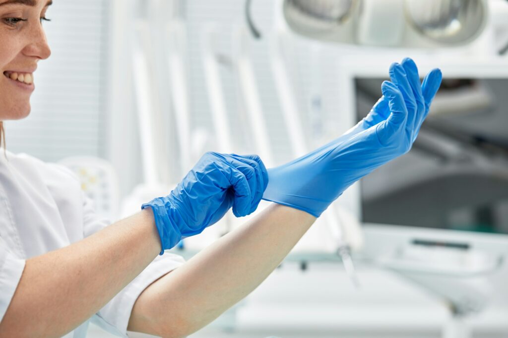 A female dentist puts on gloves against a background of dental equipment in a dental office. Happy